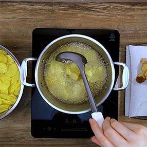 Chips aus Kartoffelschalen selbstgemachte Kartoffelchips beim Frittieren umruehren